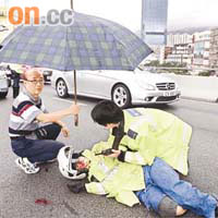 跟交通警員穿戴同款雨褸及頭盔的女鐵騎士滿面披血倒地，好心司機以車擋路，並協助打傘為傷者遮雨。	（張曉楠攝）