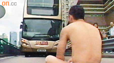 僅穿內褲的男子在路面盤膝打坐，阻礙巴士前行。	（有線畫面）