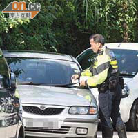 一名交通警員向違例停泊在石屎路的車輛發告票。
