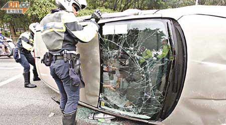 女司機被困於翻側私家車內，警員趕至施救。	（李國健攝）