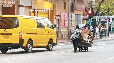 老婦於馬路中心推着滿載紙皮的手推車，路面安全成疑。