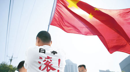 示威者穿上寫有「日本滾出釣魚島」的上衣，在日駐華使館門外揮動國旗抗議。（中新社圖片）