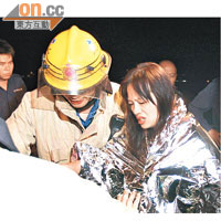 一名女乘客被救起後，表情痛苦的由消防員協助登上救護車。