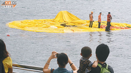 工作人員昨到已洩氣的巨鴨身上準備將它吊上岸邊進行檢查。(何天成攝)