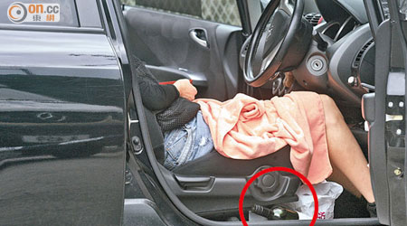 婦人在車內司機位燒炭自殺死亡，身旁留下一個空紅酒樽（紅圈）。（黃智康攝）