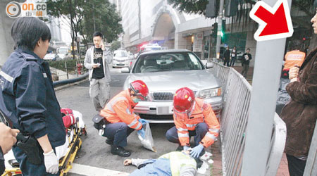 救護員拯救被私家車撞倒的女傷者，肇事女司機（箭嘴示）站在一旁觀望。（冼耀華攝）