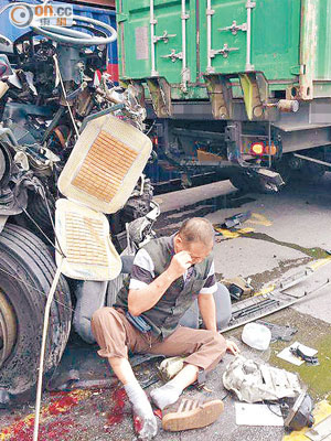 受傷司機坐在損毀的貨櫃車旁，等候送院。（網民 Yiu Gor提供）
