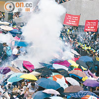 一枚催淚彈落在示威人群，眾人撐傘遮擋。