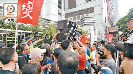 示威者將一個寫有「我們若沉默 香港將無聲」的黑箱掟入中聯辦。（蕭毅攝）