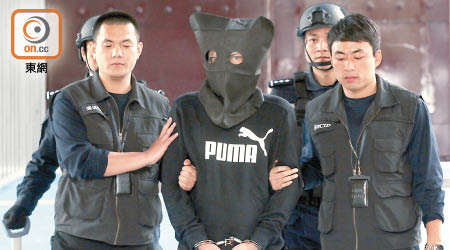 被告詹偉堅（戴頭套）日前由內地當局移交香港警方後，昨被正式檢控。