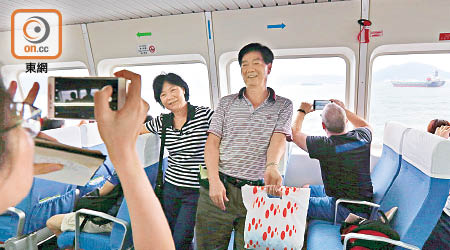 愉景灣渡輪上，乘客劉先生（右二）及太太（右三）用遼寧號作背景拍照。（洪業銘攝）