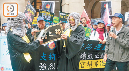 保衛香港運動成員扮演兩名法官用磚掟爛寫有「法治之都」的道具。（徐家浩攝）