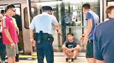 涉案男子坐在月台幕門前，有警員持警棍戒備。（互聯網圖片）