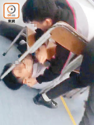 一名男生被七、八名同學用兩張椅子困在椅下，動彈不得。（互聯網圖片）