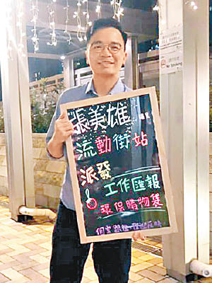 張美雄喺港鐵站舉住螢光黑板，派工作報告同環保袋畀街坊。（互聯網圖片）