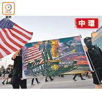 參加中環集會的黑衣人展示美國國旗及印有美國總統特朗普與坦克的旗幟。（黃仲民攝）