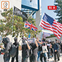 有蒙面科大生在遊行期間揮舞美國旗及英國旗。（陳錦燕攝）