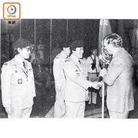 1977/07/30<br>當年駐港三軍司令夏卓賢爵士（右）授旗予香港童軍慶祝英女王登基銀禧紀念出訪星、馬、泰及印尼等國的名譽領隊馬惜珍先生（前中）。